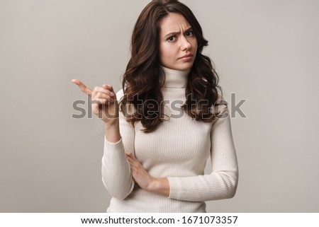 Photo of caucasian serious woman with long brown hair pointing at copyspace isolated over beige background Royalty-Free Stock Photo #1671073357