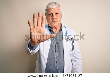 Senior handsome hoary doctor man wearing coat and stethoscope over white background doing stop sing with palm of the hand. Warning expression with negative and serious gesture on the face.