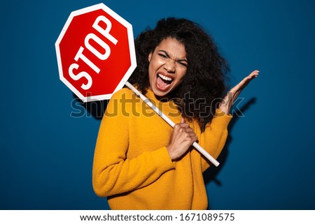 Image of a pretty displeased angry screaming african woman posing isolated over blue wall background holding stop symbol sign.
