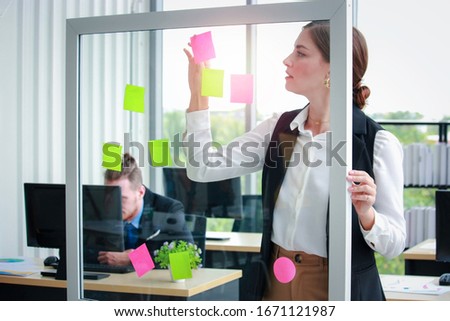 Young beautiful successful business woman wrinting her idea on post-It sticky note paper, working in office, critical thinking in project work Royalty-Free Stock Photo #1671121987