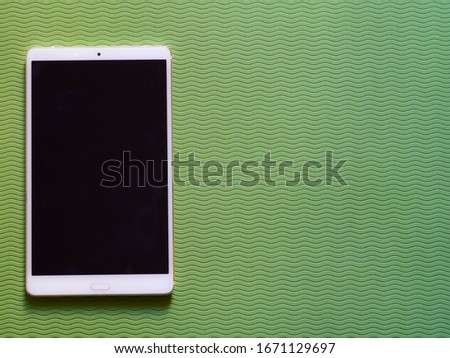 Blank for lettering call to action. Black tablet screen lying on left side of a flat green table background. Use in mobile marketing, advertising communication technologies, mobile services. Top wiew.