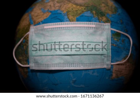 The green surgical mask wrap on the globe model the conceptual image of health , influenza and  a viral infection   , COVID -19 