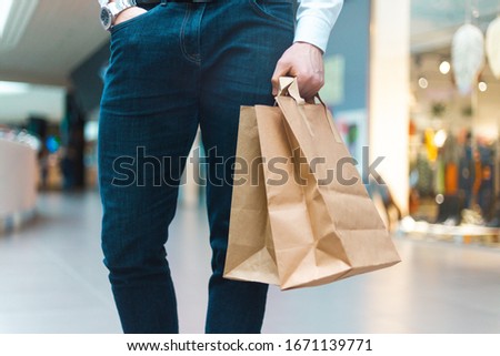 Closeup of a young stylish man walking in a mall with ecology friendly shopping bags in hand with goods and clothes. Sales, discount sold out concept. Seasonal sell out