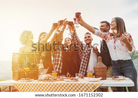 Group of friends making a toast during a barbecue in the countryside - Happy people having fun at a picnic on the hills in summer at sunset