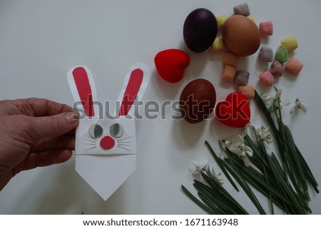 A hand holds an Easter Bunny against a background of eggs and snowdrops