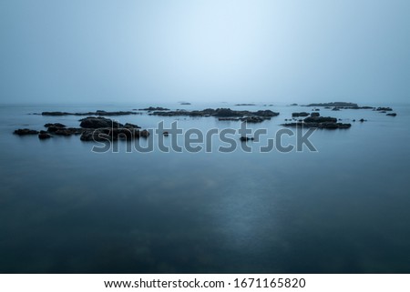 A long exposure seascape photographed on an overcast day in the small fishing village of Port Nolloth, South Africa, with a misty sea enveloping the rocks.