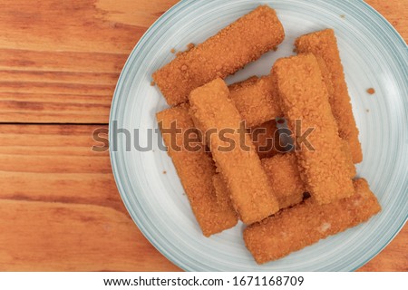 Fried fish sticks on the plate above wooden background