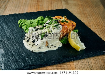Serving of grilled salmon steak in cream-cheese sauce and mashed green peas garnished. Close up, selective focus