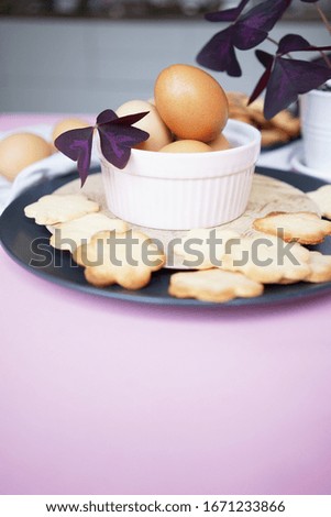                                
still life in easter style - eggs in a bowl decorated with pink clover and cookies in the shape of flowers on a pink background