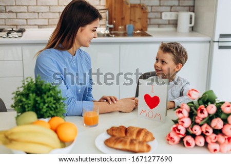 Happy mother's day! Small son congratulates his mother and gives her a postcard and flowers tulips on kitchen