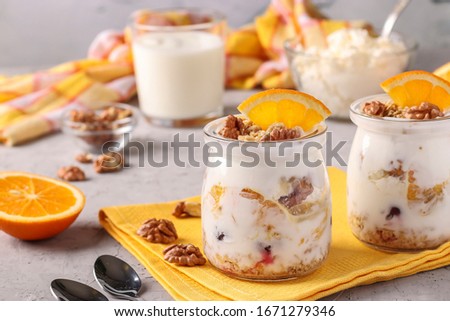 Granola crispy honey muesli with natural yogurt, frozen berries, oranges and nuts in glass jars on a gray background, healthy food, Closeup