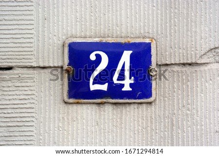 House Number 24 sign. Blue enamelled Number twenty-four plate mounted on a stucco wall.