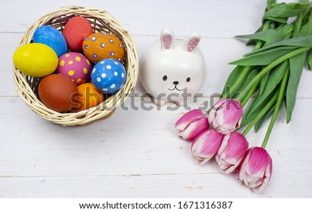 Easter eggs. Multi-colored Easter eggs with tulips and a rabbit on a white wooden background. Eggs in the basket. Banner. Tulips. Copy space
