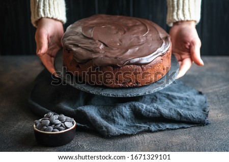 Female hands with chocolate cake with icing and apples on a dark background.
