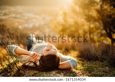 Carefree happy woman lying on green grass meadow on top of mountain enjoying sun on her face.Enjoying nature sunset.Freedom.Relaxing in mountains at sunrise.Sunshine.Daydreaming.Listening to music Royalty-Free Stock Photo #1671354034