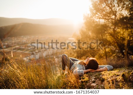 Carefree happy woman lying on green grass meadow on top of mountain enjoying sun on her face.Enjoying nature sunset.Freedom.Relaxing in mountains at sunrise.Sunshine.Daydreaming.Listening to music Royalty-Free Stock Photo #1671354037