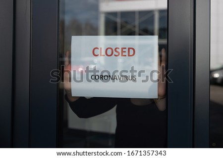 Woman hangs a card with information about the store closing on a shop window due to the coronavirus Royalty-Free Stock Photo #1671357343