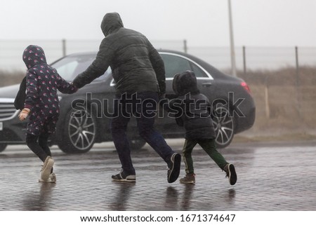 picture of a family who is crossing a street while it is heavy raining