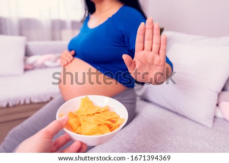 Stop to the junk food during pregnancy. Pregnant woman refuses to eat unhealthy chips.   Royalty-Free Stock Photo #1671394369