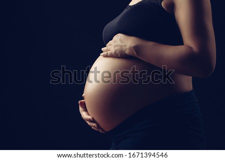 Subtle light revealing pregnant woman, holding belly with two hands. Royalty-Free Stock Photo #1671394546