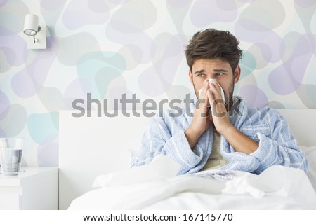 Sick man blowing his nose while sitting on bed at home Royalty-Free Stock Photo #167145770