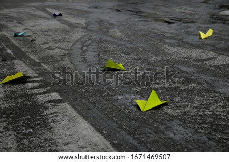 Light green thrown away paper plane on empty wet city street rainy weather dark black road asphalt surface texture