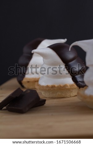 cupcakes in the shape of funny penguins of meringue with chocolate over wood piece on black background