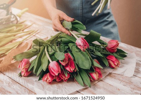 Hands of young woman florist working with fresh flowers making bouquet of pink roses on table. Close up.
