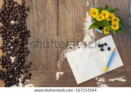Yellow flower and coffee bean on old wood with paper note and pencil.