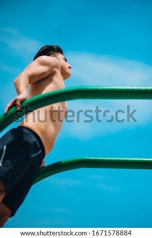 Handsome young man doing street workout on the beach on chin up bar