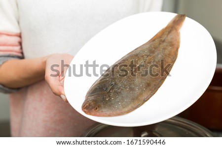 Closeup of whole fresh black sole fish on plate in hands of woman

