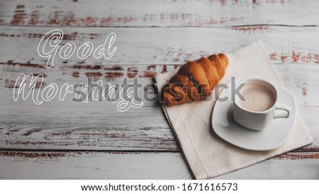 Greeting card with the inscription Good morning. A Cup of coffee and a croissant on a white wooden table