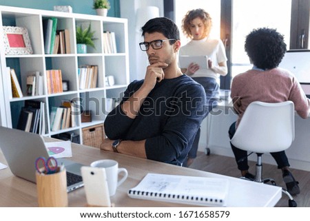 Shot of handsome young entrepreneur using the laptop while his colleagues working together in the office.