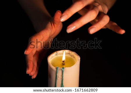 Mysterious magic close-up - women's hands conjure over a burning candle in isolation on a black background. The concept of prediction, clairvoyance and divination