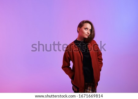 Attractive hipster girl on color background. Portrait of gorgeous female model posing in fashion color clothes in studio. Beautiful trending neon background.