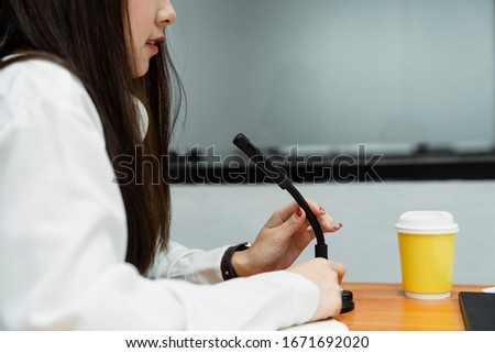 Cropped image of black microphone is held by woman podcaster on the wooden table with yellow cup of coffee.