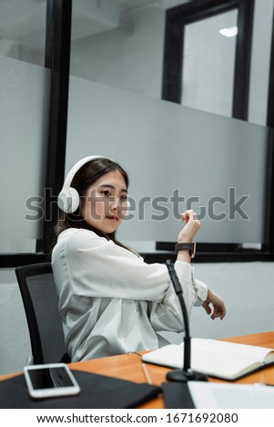 Black long hair podcaster girl in white shirt wearing white headphone stretching her arms during breaking time of broadcasting.