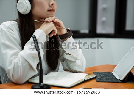 Thoughtful working woman sitting in a studio with pencil in her hands and headphone on her head.