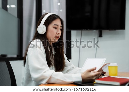Black long hair podcaster girl in white shirt wearing white headphone use smartphone during breaking time of broadcasting.