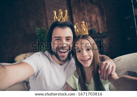 Closeup photo of little funny lady her handsome daddy friendship sit comfy sofa making taking selfies hugging wear golden crowns celebrities famous person house room indoors