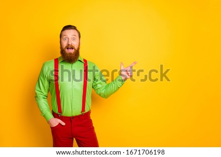 Photo of attractive amazed guy indicate finger empty space presenting black friday shopping season opening wear green shirt red suspenders pants isolated yellow color background