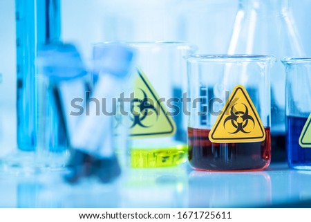 Beaker of sample test, red liquid solution in container with biological hazard warning sticker in laboratory. Idea for science research of contagious disease, virus or other infective pestilence. Royalty-Free Stock Photo #1671725611