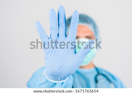 A young doctor in medical uniform with a protective face mask and a gloved hand showing a stop sign . Medical infects stopping concept. Stop COVID-19 concept.