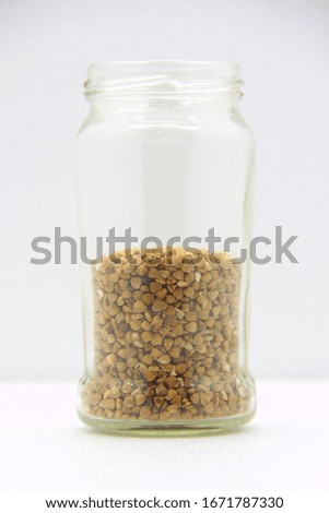 Glass jar with buckwheat on a white background, side view. The concept of healthy nutrition, diets, vegetarian products. Stock photo with empty space for text and design.
