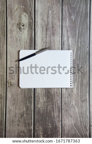Notepad with a blank white sheet in a checker paper with ball pen lies on the background of wooden boards.