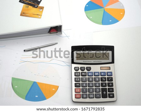 Top view of office desk.It have silver pen, gray calculator,business chart ,folder and credit plastic card lie on table for business accounting.
