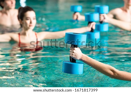 Selective focus of trainer with barbell working out with people in swimming pool Royalty-Free Stock Photo #1671817399