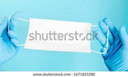 Hands in blue gloves hold a medical white mask on a blue background. Medicine concept. Wide format, copy space. Protection concept.