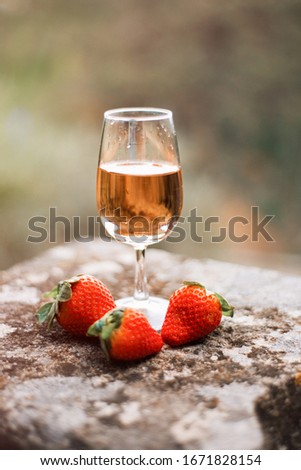 Vertical picture of glass of rose wine and three strawberries on stone wall in evening sunset time in heart of Provence, France, famous travel tourism destination