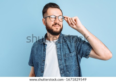Attractive smart man in glasses, in casual clothes posing standing on an isolated blue background